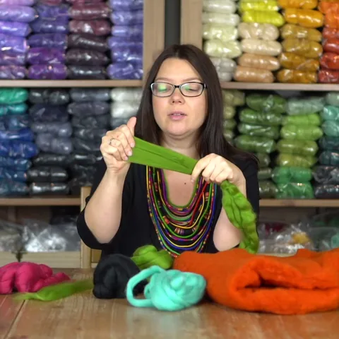 Bonus: Justyna holding up a length of green merino wool in front of shelves of colorful felting wool