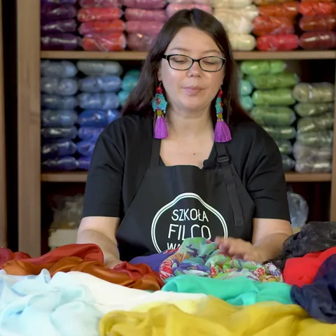 Module 1: Justyna behind a table piled with silks and other fabrics in many colors