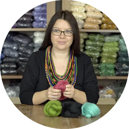 Justyna Wróbel-Mikołajczyk, felting teacher, holding a tuft of pink wool in front of shelves of felting wool